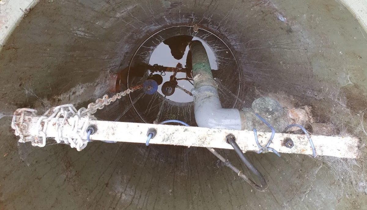 Looking down into an open drainage chamber, with pipework and a chain ladder visible below ground